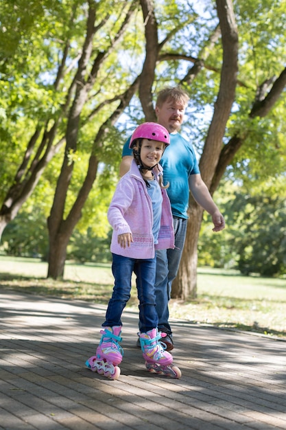 아빠는 딸에게 공원에서 롤러 스케이트를 가르친다