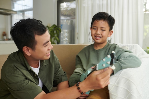 Dad teaching son playing ukulele