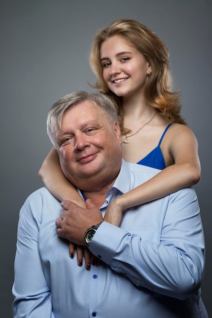 Dad and teenage daughter hug and smile A girl in a blue dress a man in a blue shirt Love and tenderness Grey background Vertical