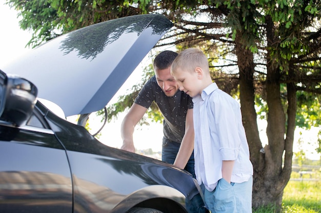 Dad tells his son the device of the car under the hood on the street
