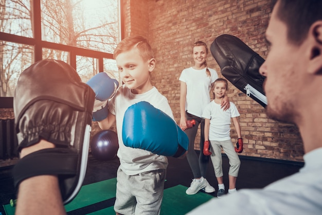 Dad trains little boxer in gloves in gym.