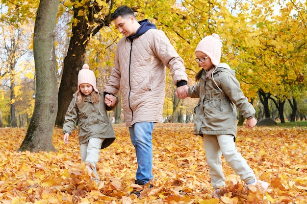 秋の公園で双子の娘たちと歩くお父さん 横写真