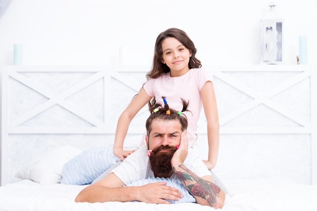 Dad who trapped at home with coronavirus quarantine and kid Family leisure Pajamas party Happy childhood Relaxing in bedroom Girl making hairdo for dad Quarantine with children Happy family