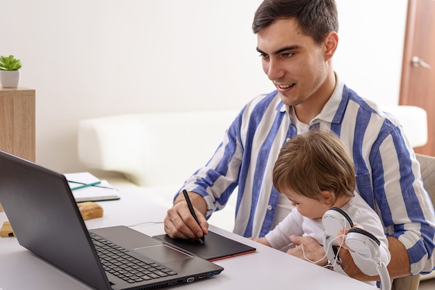 Papà con bambino in braccio, lavoro a distanza a casa sul laptop