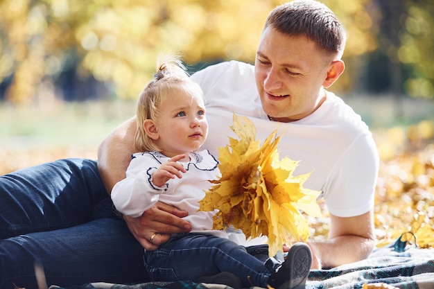 Dad with little daughter have a rest in an beautiful autumn park at sunny day.