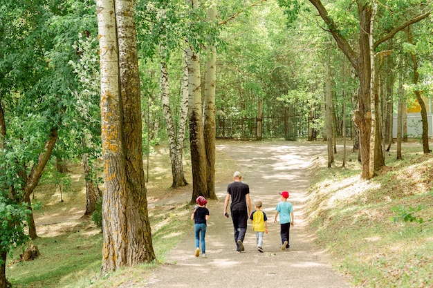 사진 공원에서 산책 하는 세 자녀와 아빠입니다. 아빠, 두 아들과 딸 자연. 가족의 편부모. 아이들과 아빠의 날. 아이가 많은 아빠.