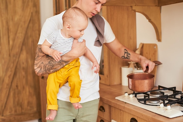 A dad with a young son in his arms prepares dinner