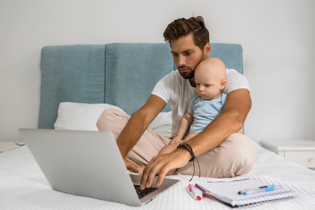 Foto papà che lavora al laptop da casa durante la quarantena con il bambino