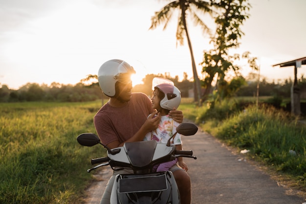 Daddy help her daughter to fasten the helmet