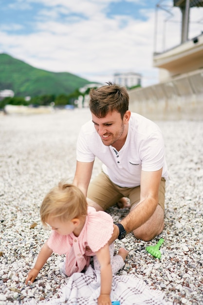 Papà tiene in braccio una bambina che striscia sulla spiaggia di ciottoli