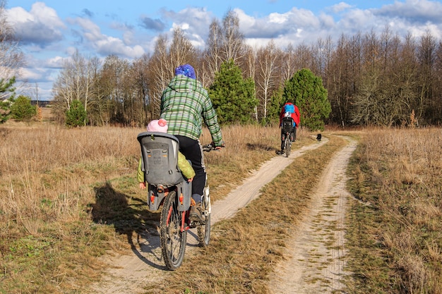 Dads ride their daughters on bicycles on a dirt road through a birch forest