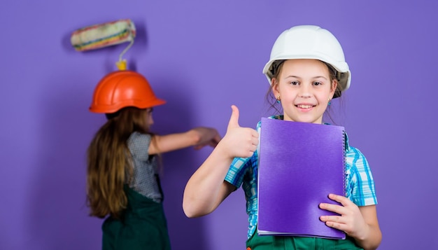 Dag van de arbeid 1 mei Muur schilderen Voorman inspecteur Reparatie technisch idee Toekomstige carrière kleine meisjes samen repareren in werkplaats Kleine kinderen in helm met tablet en roller beste expert