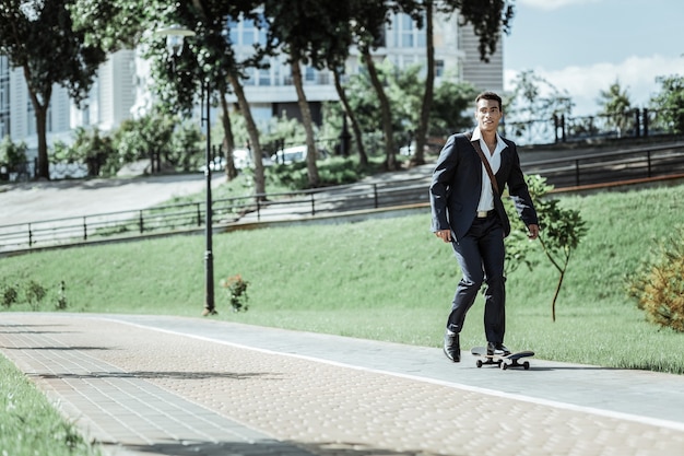 Dagelijkse training. Actieve mannelijke student rijden op skateboard en pak dragen