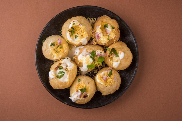 Foto dahi puri è uno snack popolare nello stato del maharashtra, in india. questo piatto rientra nella categoria chat. servito in un piatto rotondo su sfondo colorato o in legno. messa a fuoco selettiva