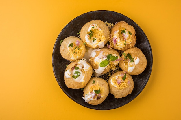 Dahi puri è uno snack popolare nello stato del maharashtra, in india. questo piatto rientra nella categoria chat. servito in un piatto rotondo su sfondo colorato o in legno. messa a fuoco selettiva