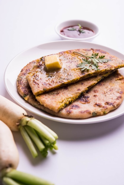 Daikon of Radijs of Mooli gevulde Paratha geserveerd in een bord met boter en tomatenketchup, over kleurrijke of houten achtergrond. selectieve focus