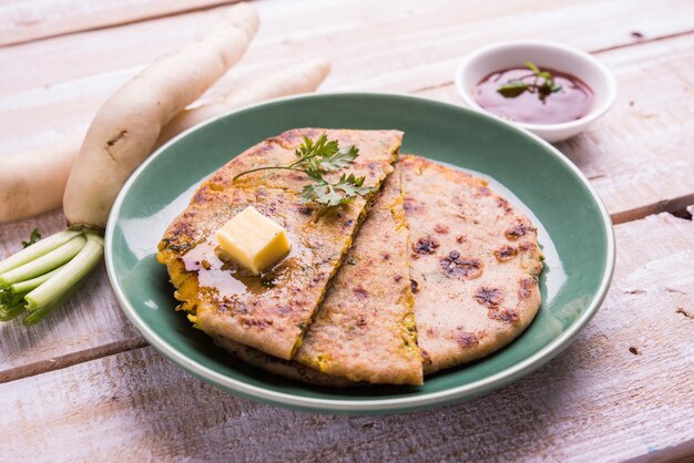 Daikon 또는 Radish 또는 Mooli 박제 Paratha는 다채로운 또는 나무 배경 위에 버터와 토마토 케첩을 곁들인 접시에 제공됩니다. 선택적 초점