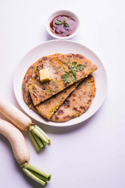 Daikon 또는 Radish 또는 Mooli 박제 Paratha는 다채로운 또는 나무 배경 위에 버터와 토마토 케첩을 곁들인 접시에 제공됩니다. 선택적 초점