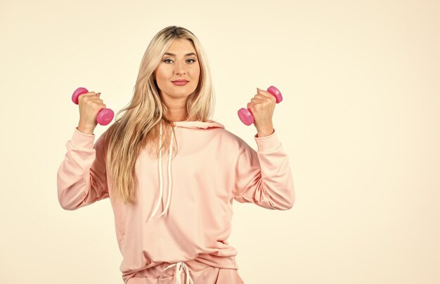 Ежедневные упражнения Фитнес-девушка поднимает гантели Женщина в спортивной одежде держит гантели Фитнес-оборудование Розовый - ее любимый Оставайтесь в форме Здоровая фитнес-женщина делает упражнения с гантелями