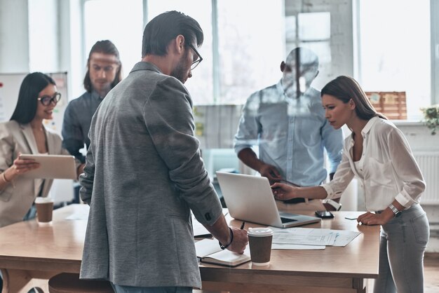 Daily meeting. Group of young modern people working and communicating together while standing behind the glass wall in the board room