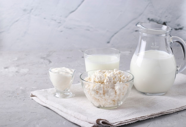 Dairy products: milk, kefir or ayran, cottage cheese and sour cream in a transparent bowl, jug and glass on a gray surface, space for text, Closeup