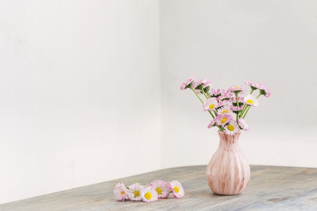 Daisy flowers in pink vase on wooden table