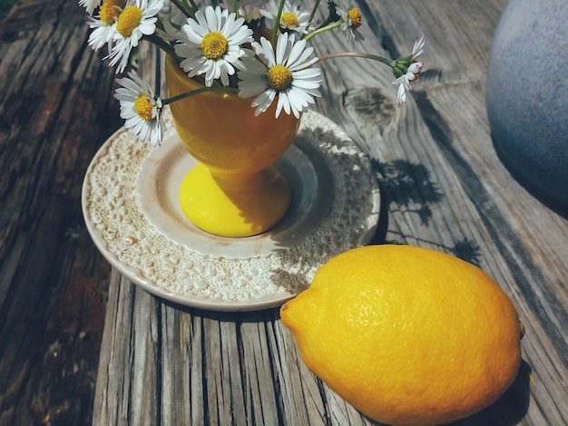 Photo daisy  fresh wild flowers in yellow ceramic vase whole lemon on wooden veranda background