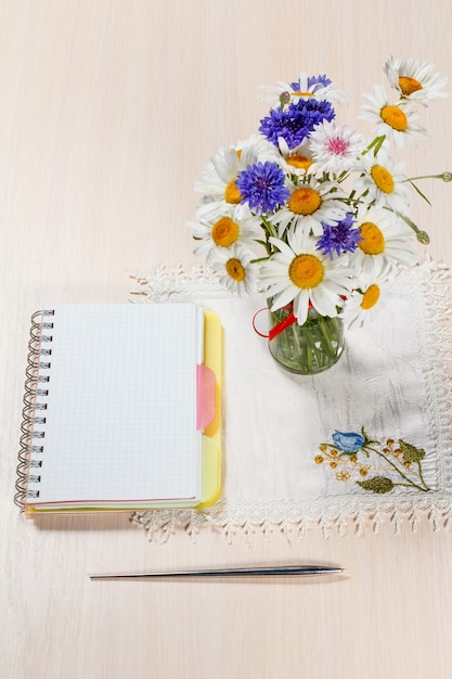 Daisy kamille en korenbloemen in vaas op een houten tafel met een notitieboekje en een pen