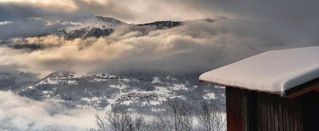 Dak van een besneeuwd houten chalet met uitzicht op de alpine berg in de winter en bewolkte hemel