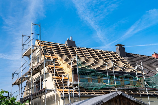 Dak van een woongebouw omgeven door steigers om nieuwe tegels onder de blauwe lucht te bedekken