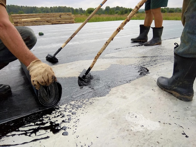 Dakdekkerswerker schildert bitumen praimer op betonnen oppervlak door de rolborstel Waterdichting