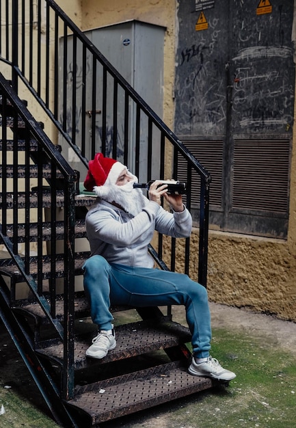 Dakloze kerstman die wijn drinkt en door vuilnisbakken snuffelt.