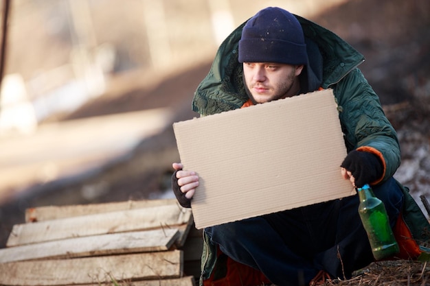 Dakloze man houdt blanco karton vast voor je tekst
