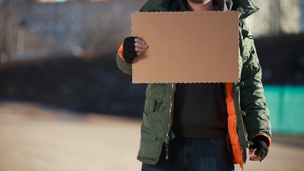 Dakloze man houdt blanco karton vast voor je tekst