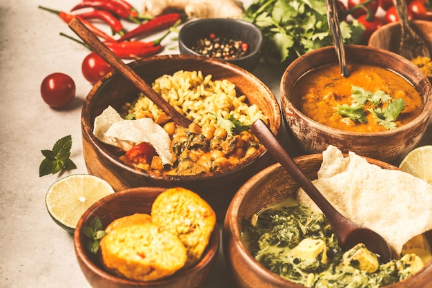 Photo dal, palak paneer, curry, rice, chapati, chutney in wooden bowls on white table.