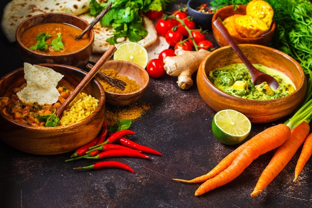 Dal, palak paneer, curry, rijst, chapati, chutney in houten kommen op donkere tafel.