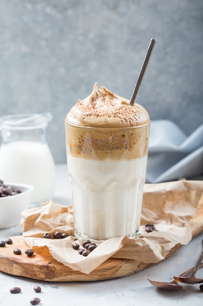 Foto caffè cremoso dalgona in un bicchiere su uno sfondo grigio chiaro con schiuma montata. tendenza alimentare coreana, formato verticale