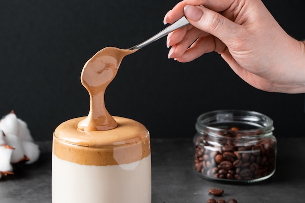 Dalgona-koffie Trendy drankje op zwarte achtergrond Vrouw zet pluizig zoet schuim in glas met melk