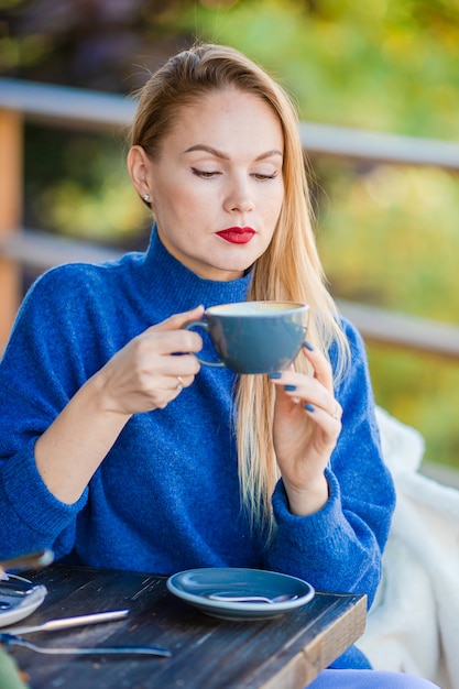 Dalingsconcept - mooie vrouw het drinken koffie in de herfstpark onder dalingsgebladerte