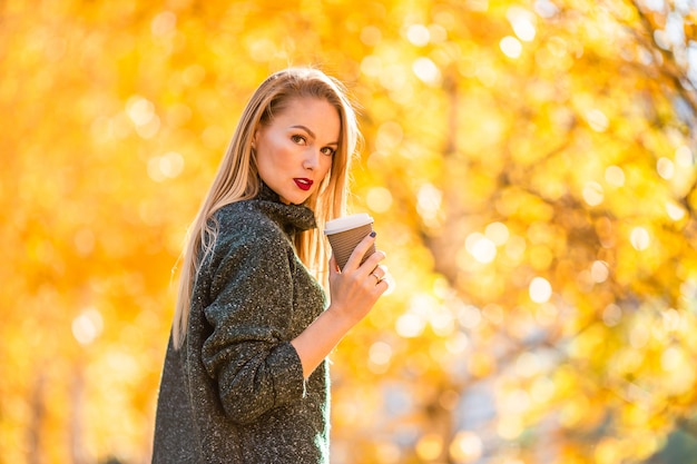 Dalingsconcept - mooie vrouw het drinken koffie in de herfstpark onder dalingsgebladerte