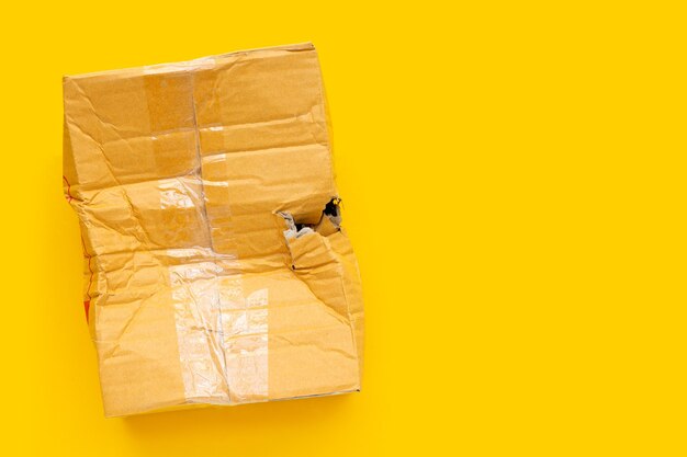 Photo damaged cardboard box with hole on yellow background.