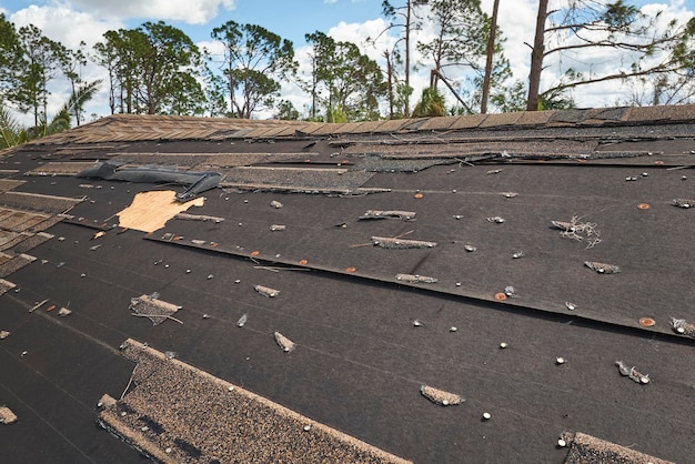 Damaged house roof with missing shingles after hurricane Ian in Florida Consequences of natural disaster