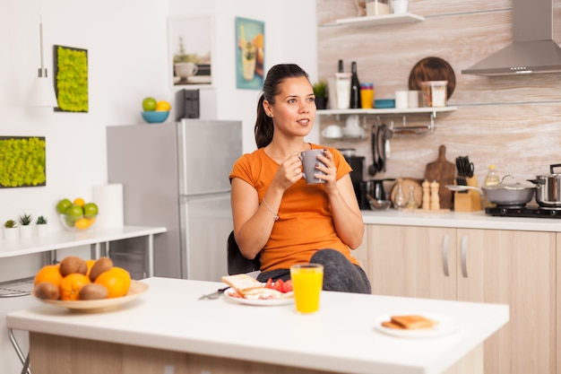 Dame geniet van een kopje koffie midden op de dag in haar keuken