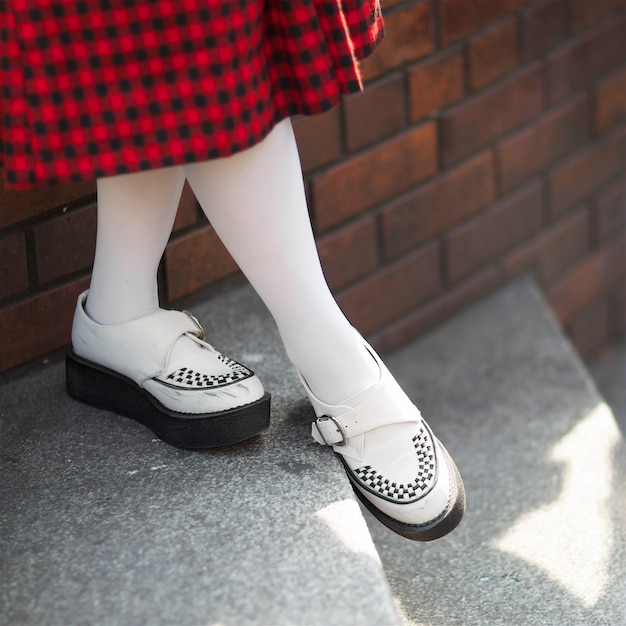 dame in punk rock stijl schoenen, zwarte en rode tartan patroon rok, witte sok met ondiepe scherptediepte, focus op schoen