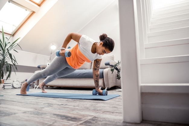 Dame met behulp van halters. Geconcentreerde jonge sportieve vrouw handen met halters opheffen tijdens het maken van plank op yogamat