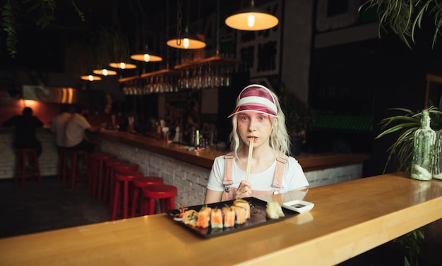 Dame met een roze pet zit aan een tafel in een japans café met een bord sushibroodjes en eetstokjes