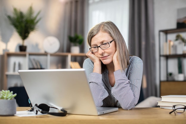 Dame van middelbare leeftijd die zich thuis moe voelt voor de laptop