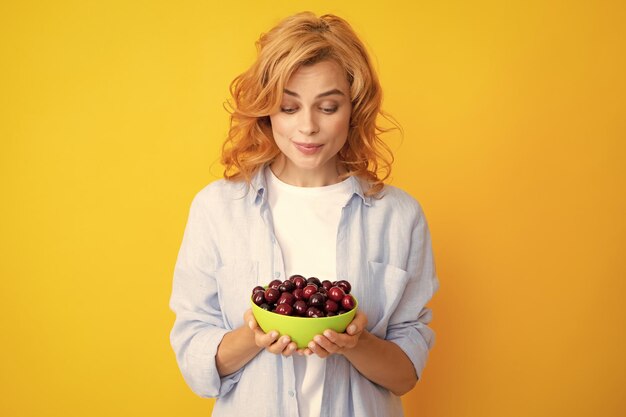 Dames genieten van een verse zoete kers Vrouw die kersen eet op gele achtergrond