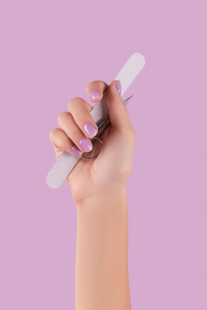 Dames hand met manicure instrument op pastel lavendel achtergrond