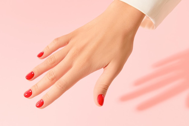 Dames hand met rode manicure op roze achtergrond. Minimalistisch nagelontwerp. Schoonheidssalonconcept